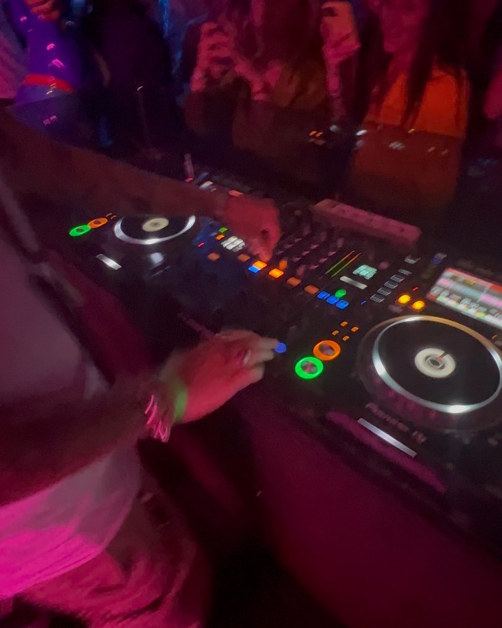 Close-up of a DJ console under magenta club lights.